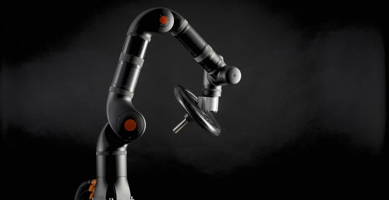 Das Bild zeigt einen industriellen Roboterarm in Aktion, der ein Metallteil hält, vor einem dunklen Hintergrund.