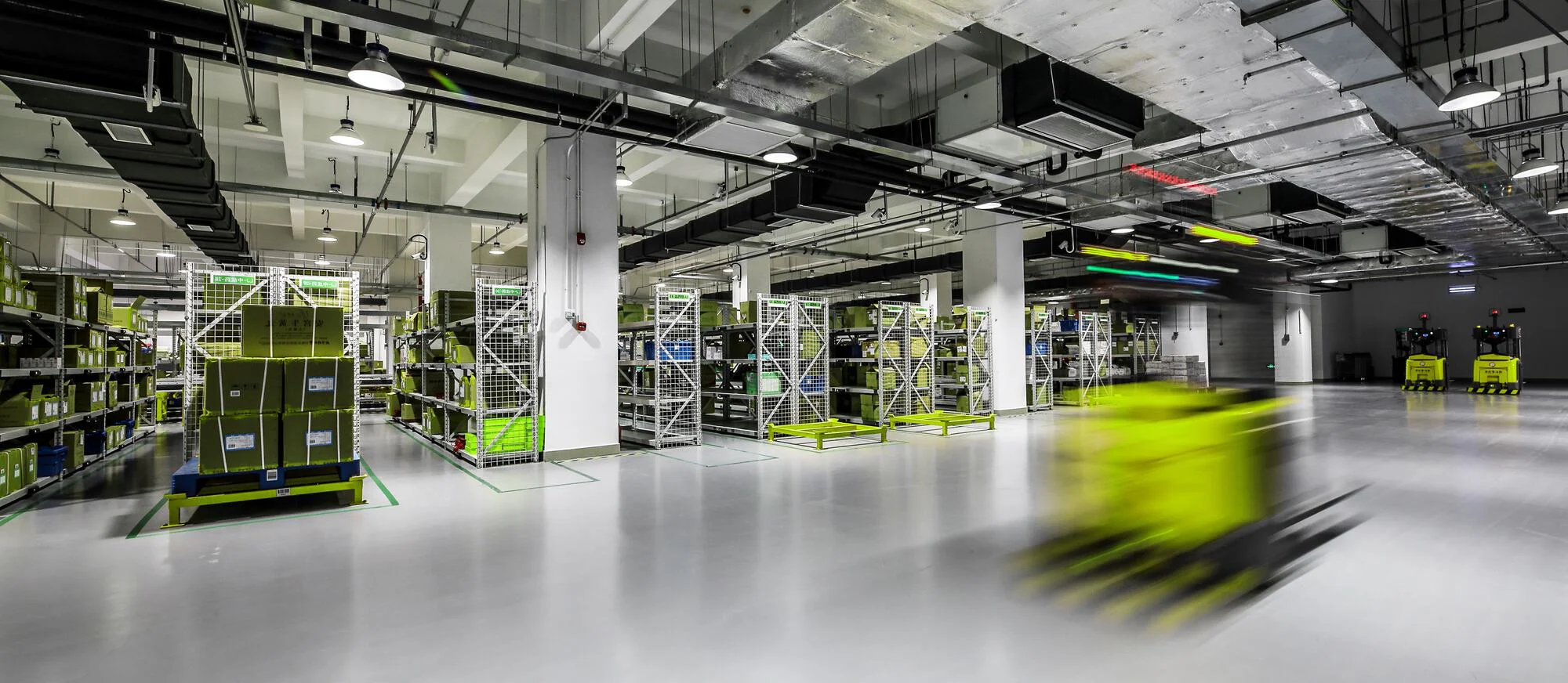 Auf dem Bild ist ein modernes Lager mit leuchtend gelben, beweglichen Automatisierungsrobotern zu sehen, die sich zwischen Lagerregalen bewegen.
