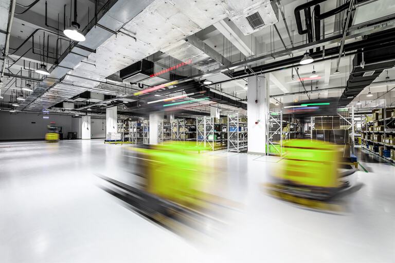 Das Bild zeigt eine moderne Lagerhalle mit leuchtend grünen automatisierten Transportsystemen von AgiloX, die in einer ansonsten neutralen, gut beleuchteten Umgebung auffallen.